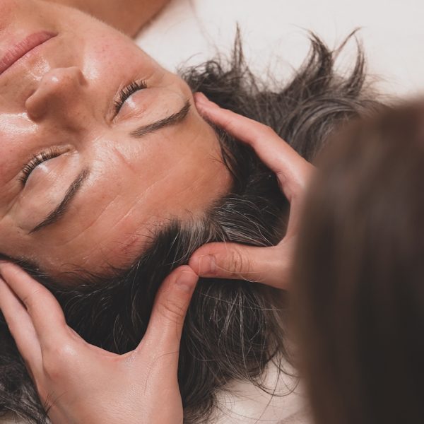 Terapeuta realiza un masaje relajante en el cabello de una mujer que se encuentra en un estado de relajación.